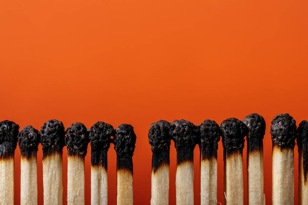 Row of burnt matches. Many burnt  matches on orange background, closeup. Copy space.