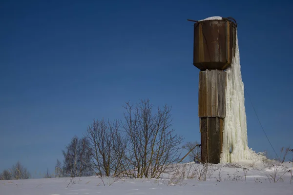 Frozen water tower in a remote village. Winter landscape. An old frozen building in the woods.