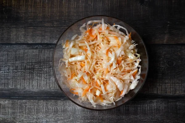 Homemade sauerkraut. Fermented food. Sauerkraut with carrots in a bowl on a wooden background. Top view, flat lay. Copy space.