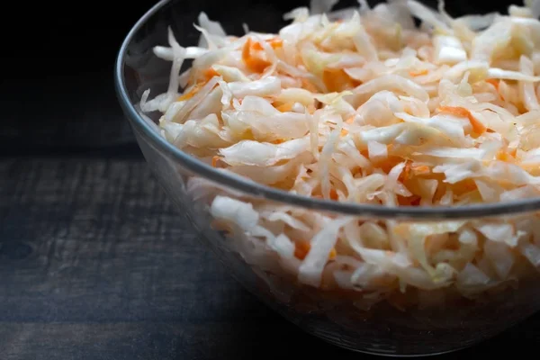 Homemade sauerkraut. Fermented food. Sauerkraut with carrots in a bowl on a wooden background. Top view, flat lay. Close up