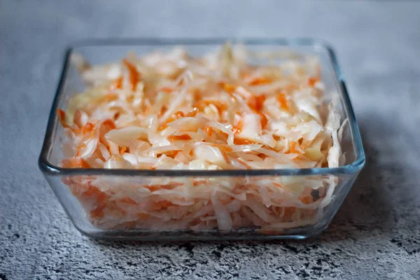 Homemade sauerkraut. Fermented food. Sauerkraut with carrots in a bowl on a concrete gray background. Top view, flat lay. Close up