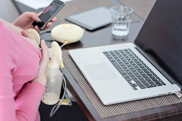 Konsep ibu yang bekerja. Memompa payudara wanita memegang ponsel dan bekerja pada laptop di rumah . — Stok Foto