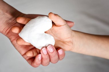 Gri arkaplanda beyaz kumaş kalp tutan iki el resmi