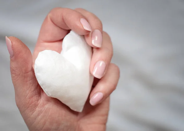 Corazón de tela blanca hecha a mano en la mano de la mujer sobre fondo gris . — Foto de Stock