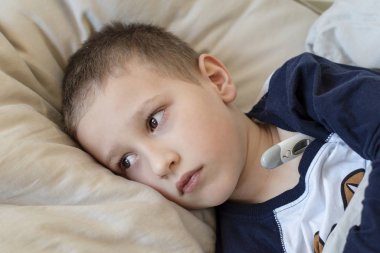 Okul öncesi hasta çocuk termometreyle yatakta yatıyor..