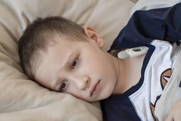 Iskola előtti beteg fiú pizsamában feküdt az ágyban egy digitális hőmérővel — Stock Fotó