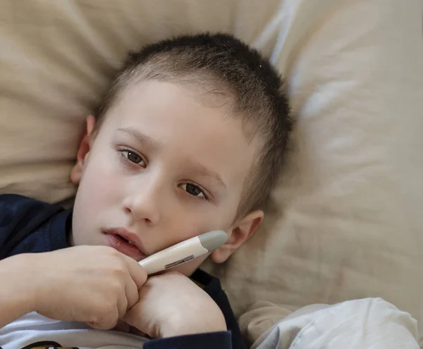 Vorschulkranker Junge liegt mit digitalem Thermometer im Bett — Stockfoto