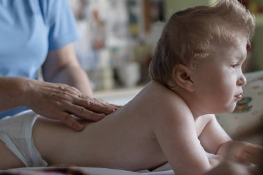 Bebek rehabilitasyon merkezinde sırt masajı yaptırıyor. Küçük çocuk terapide dinleniyor. Masaj terapisti bebeğe masaj yapıyor..