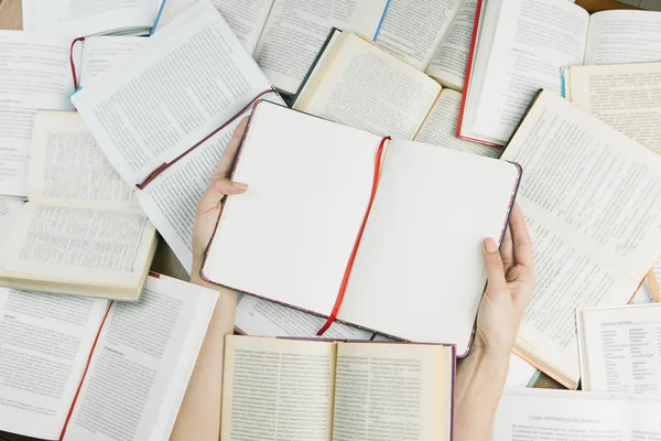 Mulher mãos segurando notebook entre um livros de pluralidade . — Fotografia de Stock