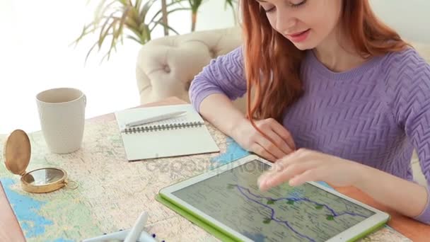 Das schöne rothaarige Mädchen betrachtet aufmerksam eine Route auf einer Karte des Tablets. v — Stockvideo