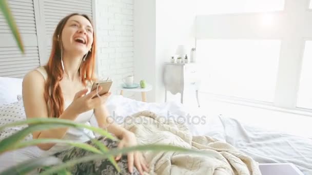 A sleepy young beautiful girl sits on bed in sleeping room — Stock Video