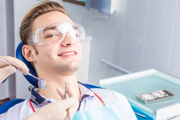 Um jovem bonito senta-se satisfeito em uma poltrona por um dentista . — Fotografia de Stock