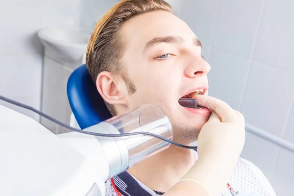 Młody facet na fotelu u dentysty sprawdza stan jego zęby. — Zdjęcie stockowe