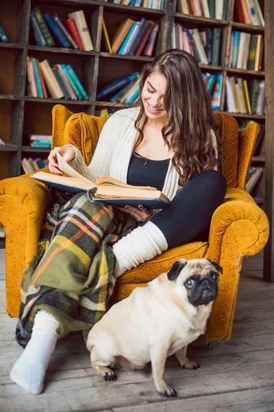 Mooie vrouw in bibliotheek en haar hond grappige pug lezen. — Stockfoto