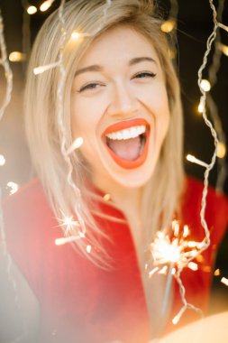 Açık ağız ile inanılmaz mutlu gülen kadın. Kırmızı dudaklar ve elbise. Yılbaşı kutlama parti havası. Maytap. sığ derinlik-in tarla