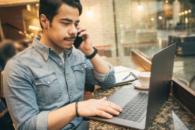 Arap adam office bilgisayar ve cep telefonu kullanarak kafede çalışıyor