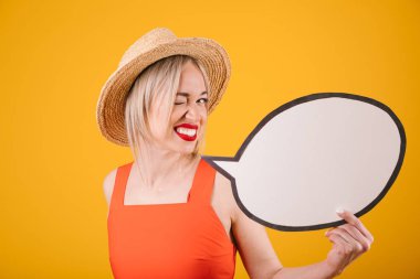 Winks sarışın kadın hasır şapka ve kırmızı kıyafet konuşma buble afiş tutuyor. Sarı arka plan