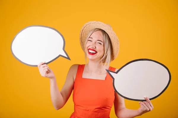Laughing adorable blonde girl in straw hat and red fancy dress is holding speech buble banners. Yellow background — Stock Photo, Image