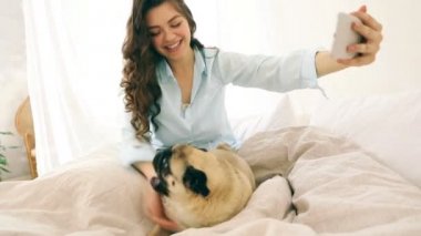 selfie ile onun küçük köpek pug alarak yatakta çekici esmer kadın. Video görüntüleri. İyi bir hafta sonu sabah ruh hali. İskambil ile komik evde beslenen hayvan