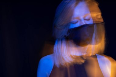 Yüz maskesi takmış genç sarışın bir kadının yaratıcı romantik portresi. Siyah, mavi ve turuncu renkler. Kapalı gözler. Rahatlamış ve yorgun. Solunum kirli havayı soluyor. Salgın panik salgını.  