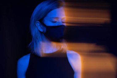 Virüs temalı. Maske takan sarışın kadın gözlerini kapadı. Dalgın meditasyon yüz ifadesi. Siyah arka plan. Uzun pozlu yaratıcı sanatsal fotoğraf serisi. Solunum kirli havayı soluyor. 