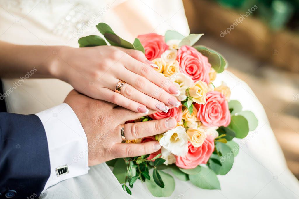 Hands of bride and groom with rings on wedding bouquet. Marriage concept.