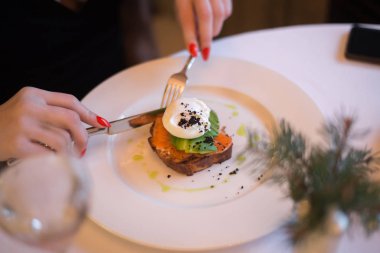 Tabak restoranda. Büyük güzel bir tabakta soslu kırmızı balık. Kırmızı manikürlü bir kızın elleri. Düzgün ve sağlıklı beslenme