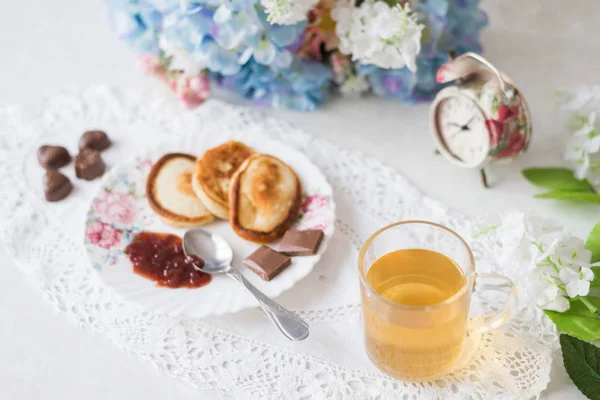 En la mesa con flores panqueques con mermelada, té verde y dulces. Vale la pena un despertador, el concepto de desayuno y dulce vida —  Fotos de Stock