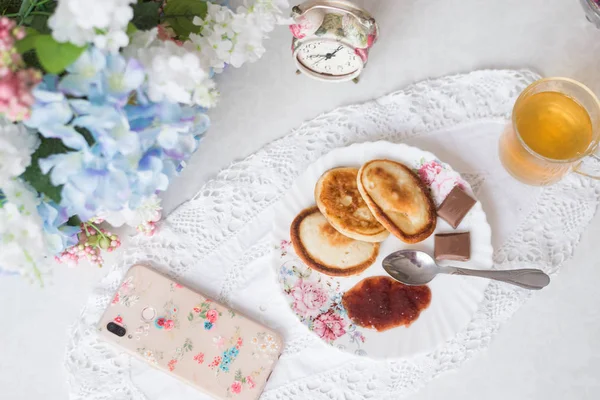 On the table with flowers pancakes with jam, green tea and sweets. Worth an alarm clock, the concept of Breakfast and sweet life — 스톡 사진