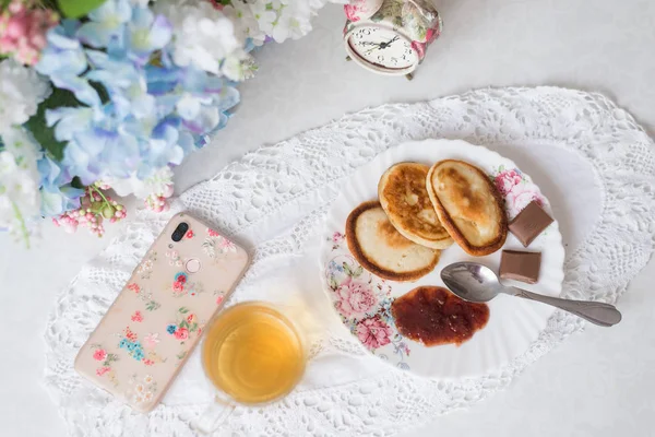 На столі з квітами млинці з джемом, зеленим чаєм та цукерками. Вартість будильника, концепція сніданку та солодкого життя — стокове фото