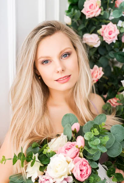 Vacker romantisk ung kvinna med naturlig makeup poserar mot en bakgrund av blommor. Flickan är blond med ett rent utseende och ett vackert leende.Närbild porträtt. Parfym och kosmetiska begrepp — Stockfoto