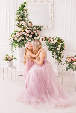 Sarışın anne ve tatlı kızı sarılıyor. Süslü kıyafetler giyiyorlar. İçi çiçeklerle dolu güzel bir yer. Prenseslerin görüntüsü. Doğum gününde ve kadınlar gününde kutlama konsepti.
