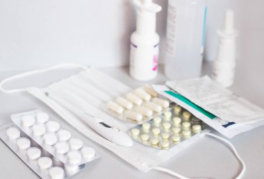 Tıbbi maske, termometre ve hafif arka planda ilaç. Soğuk algınlığı, grip ve bademcik iltihabı tedavisi.