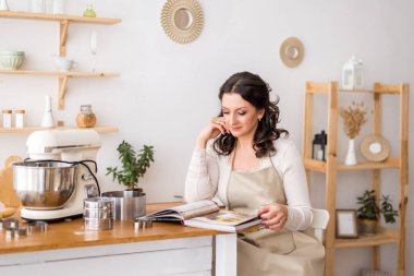 Önlüklü bir kadın yemek kitabı okuyor. Yemek pişirmeye hazırlanıyor.