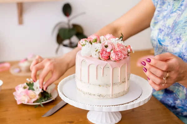 close-up of women's hands decorating the cake with fresh flowers.