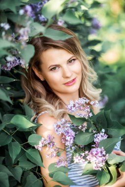 Güzel, mutlu genç bir kadın çiçek açan bir bahar leylak bahçesindeki kokunun tadını çıkarıyor..