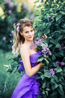 Leylak kokusunun tadını çıkaran güzel bir kadın. Şirin Model ve Çiçekler. Aromaterapi ve Bahar Konsepti. Ellerinde bir buket leylak ve saçlarında çiçekler.