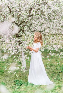 Çiçekli bir bahar bahçesinde, beyaz, uzun elbiseli güzel bir genç kız.