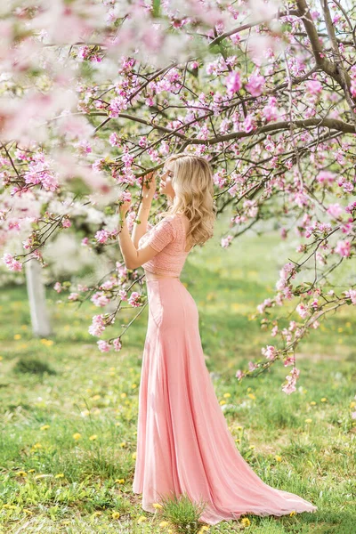 美丽的金发女子 穿着粉色长裙 在春花盛开的花园里 — 图库照片