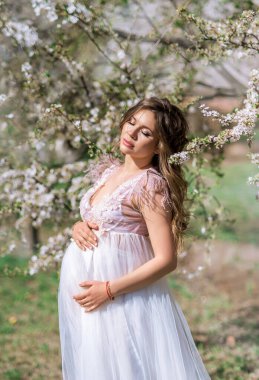 Çiçekli bir bahar bahçesinde hamile bir kadının portresi..