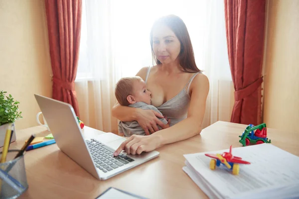 Mutlu anne laptopta çalışırken bebeği emziriyor.