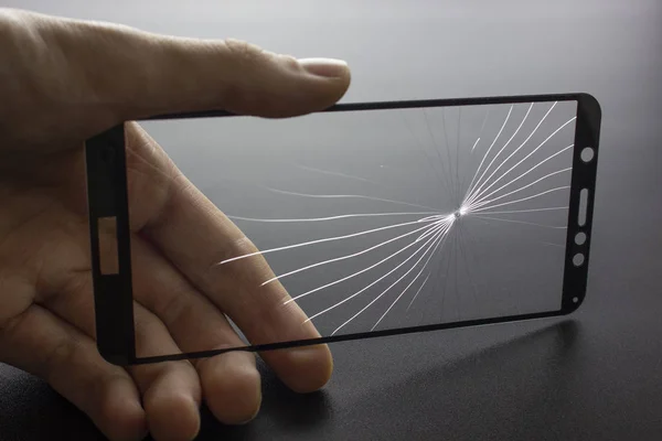 Broken protective glass of smartphone with cracks in hand on black background. — 图库照片