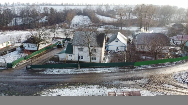 Rural two-story house, snowy spring day, bad mud road. Road problems in spring in rural area.