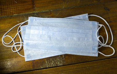 Grip ve viral hastalıklara karşı korunmak için ahşap bir masada mavi maskeli. Cerrahi koruyucu maske. Tıbbi solunum bandajları koyu arkaplanda..