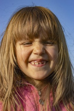 Gün batımında ön dişleri büyüyen gülümseyen küçük bir kızın portresi..