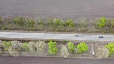 Bir arabanın geçtiği tarlaların içinden geçen tecavüzlü bir yol. Bahar güneşli hava ve yol kenarındaki ağaçlar.