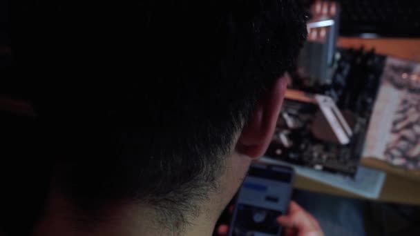 Парень смотрит обзор Интернет на смартфоне, чтобы построить компьютер и дым vape — стоковое видео