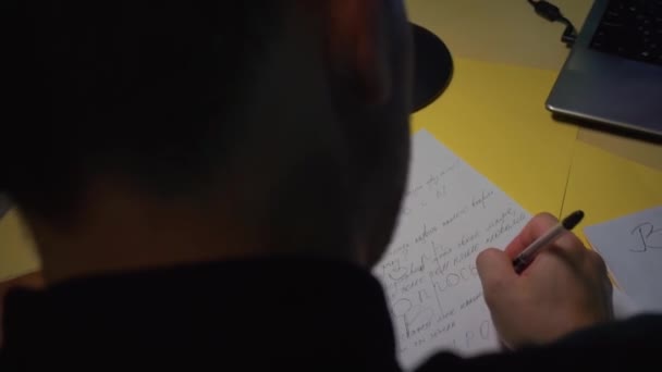 Крупним планом. Хлопець робить ноти божевільними, ручка на папері, сидячи за столом — стокове відео