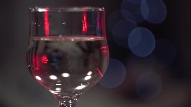 Christmas, New year, Holidays. Bubbles in champagne glass against background of flickering colored lights. Background video. Slow motion. Close up. Macro. — Stock Video