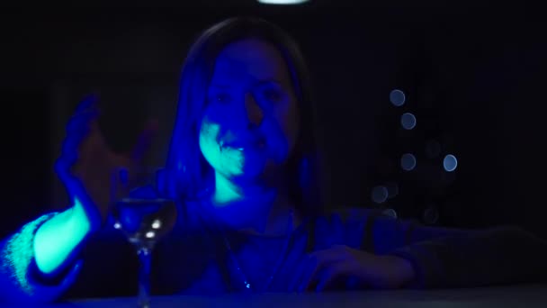 ein Mädchen in dunkelblauem Licht, mit leuchtendem Gesicht, trinkt Wein aus einem Glas